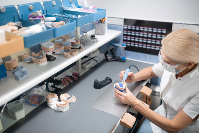 Dental technician crafting a dental model at a workstation with tools and prosthetic teeth.