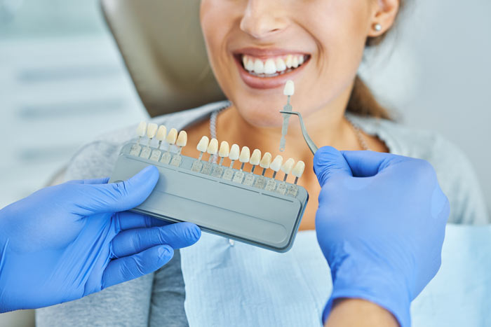 A dentist's hand holding a dental shade guide next to a smiling patient with healthy teeth, showcasing color matching for dental restoration.