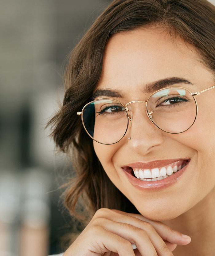 Smiling woman with glasses and a nose ring, showcasing her bright smile and healthy teeth.